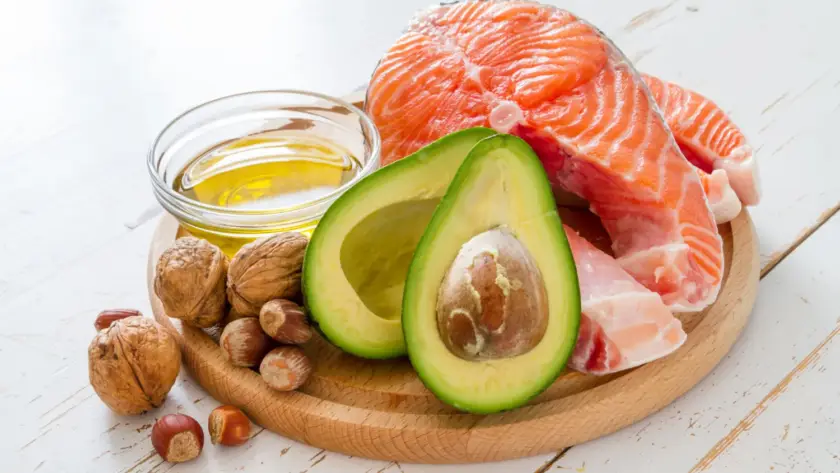 Healthy fats sources including olive oil, avocado, nuts, and seeds arranged on a wooden table