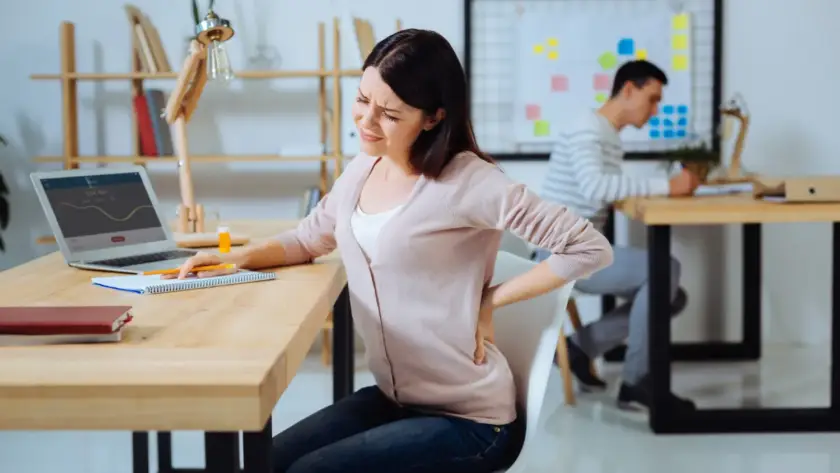 Young woman working at her office desk, experiencing back pain, highlighting the need for a Pain-Free Human Back