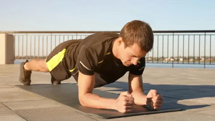 A man holding a plank position on a gym mat, engaging his core muscles during a strength-training workout.
